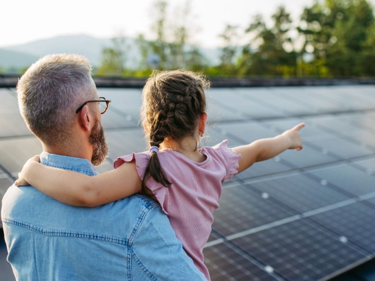 A male parent holding a little girl pointing at solar panels